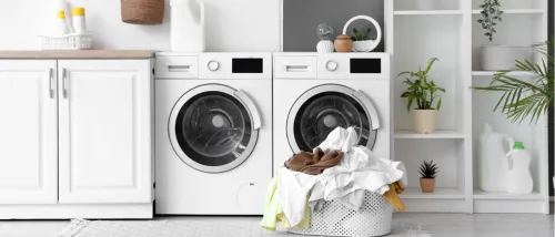 Image of a laundry room with a washer and dryer, and a basket full of clothes to illustrate how to save on utility bills while doing housework.
