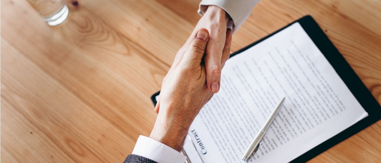 Two men shaking hands over a contract to illustrate an apartment guarantor for leases.