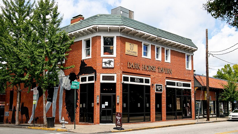 A shot of the Dark Horse tavern, a local bar in a red-brick building in Atlanta, with street art of a dog and a person painted on the side.