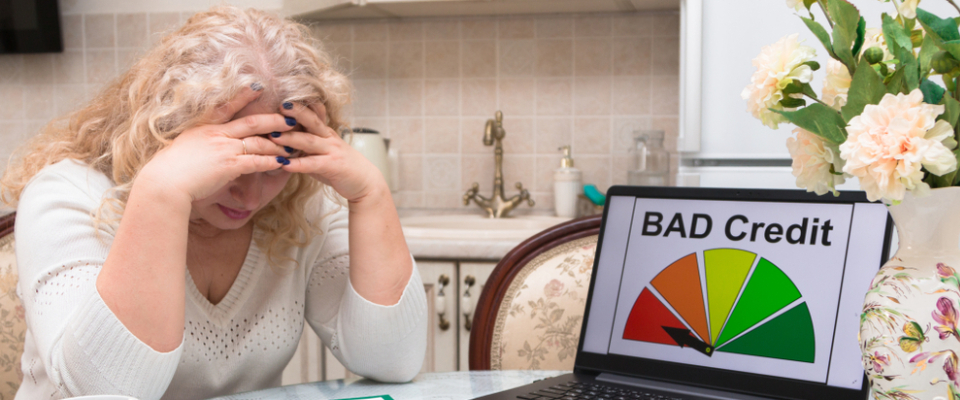 Upset renter at kitchen table viewing a bad credit score on laptop, representing the difficulty of finding bad credit apartments and affordable housing options.