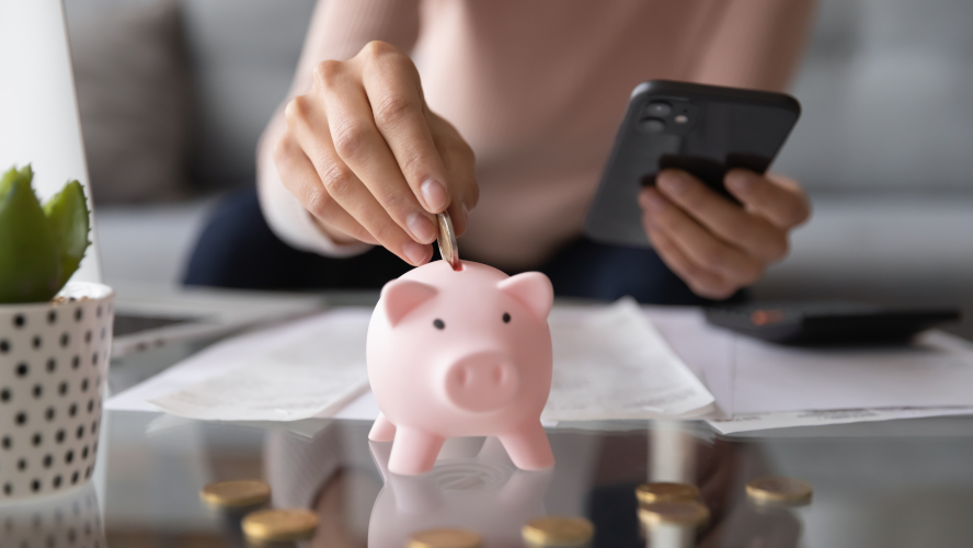 closeup person holding phone putting coin into piggy bank