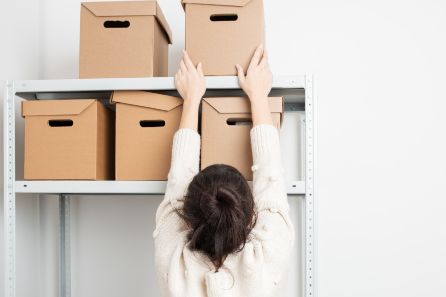person in white blouse arranging brown cardboard boxes on metallic shelves