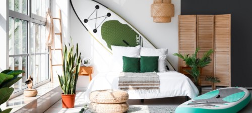 Stylish interior of bedroom with boards for sup surfing near light wall