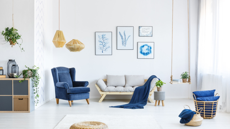 White living room with wood sofa, blue armchair, lamps, posters