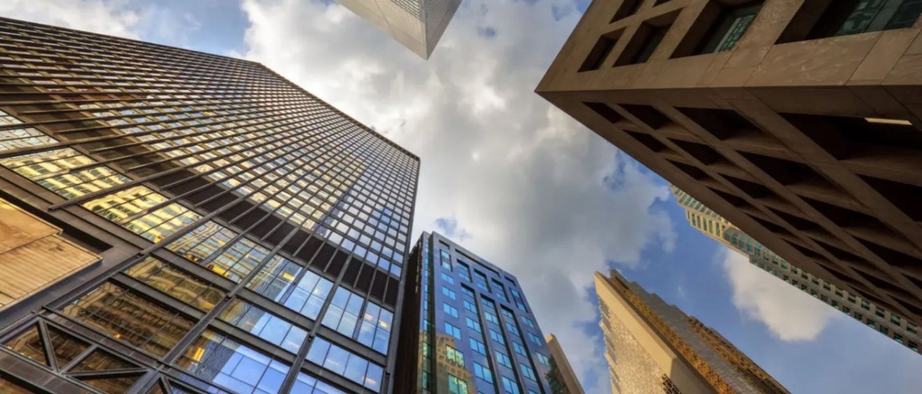Upward view of various tall office buildings with reflective glass facades against a partly cloudy sky, highlighting their impressive architecture.