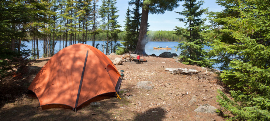 Campsite with orange tent and fire on a northern Minnesota lake during summer