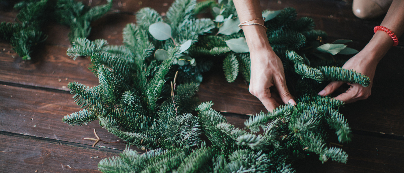two hands using evergreen twigs to create winter décor