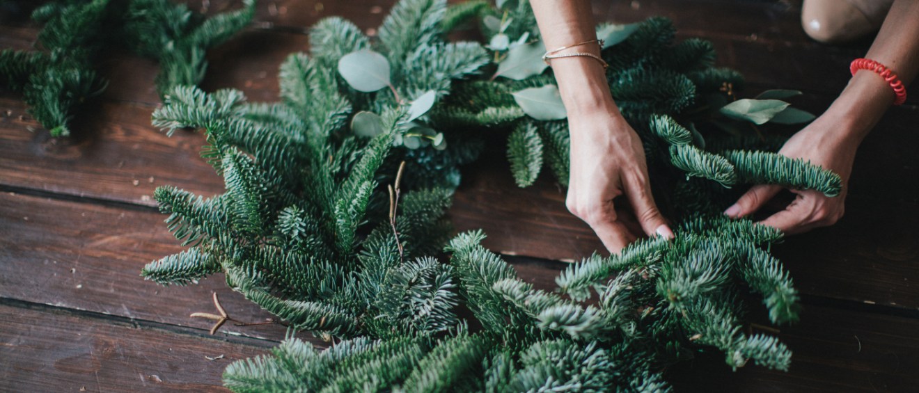 two hands using evergreen twigs to create winter décor