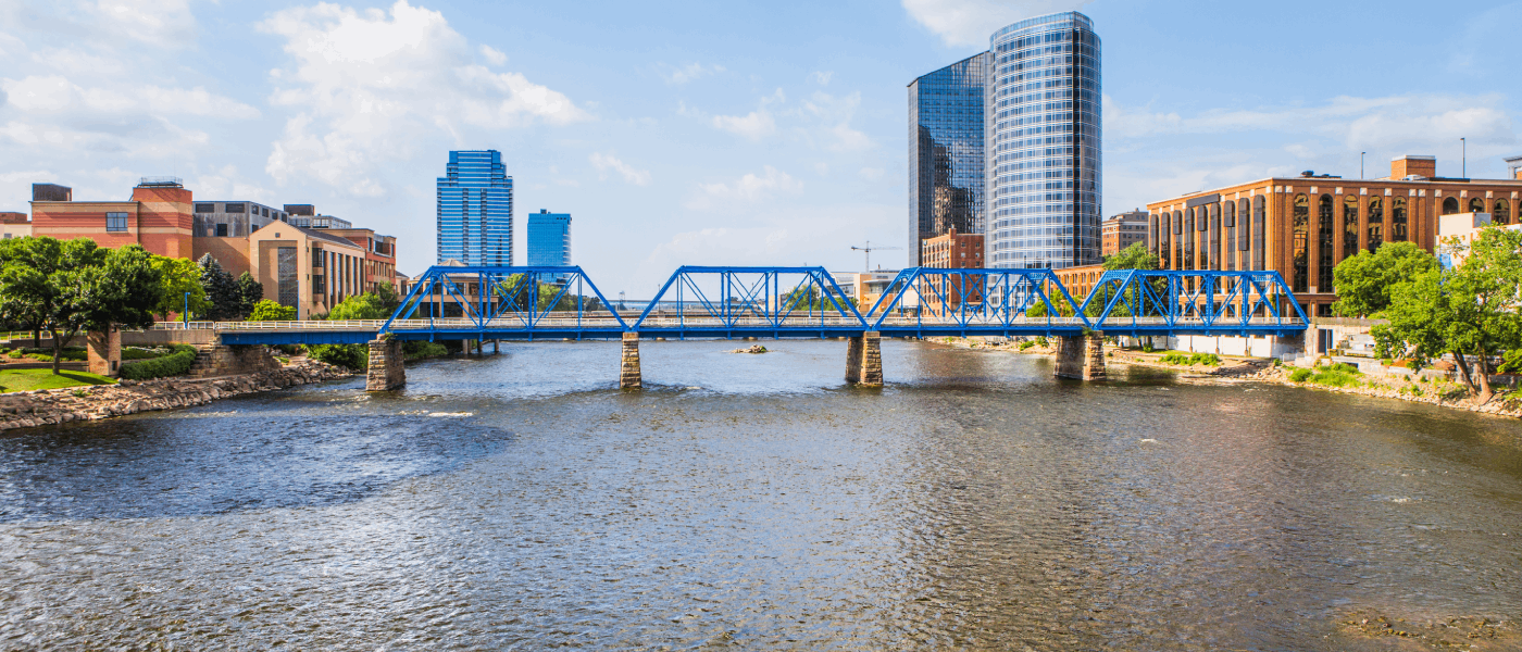 Grand Rapids skyline seen from a bridge on Grand River: skyscrapers in the distance, a bridge and the river flanked by trees in fall colors.