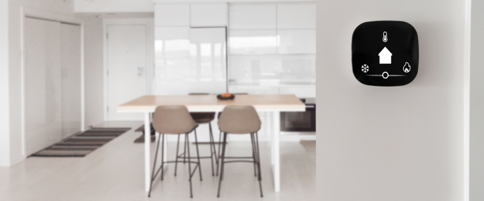 Smart thermostat device with app icons showing temperature and heat cool adjustment on a white wall inside a minimalist apartment.