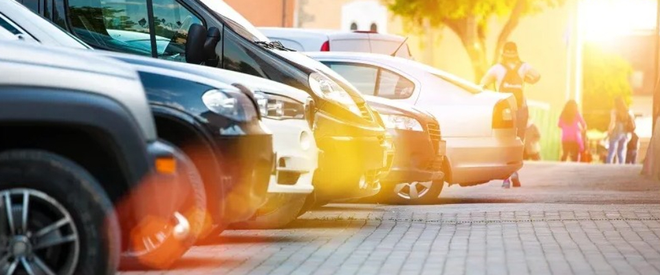 Row of cars parked closely in a city lot with sunlight flares, illustrating the demand for tandem parking solutions in congested urban areas where renters face limited parking availability.