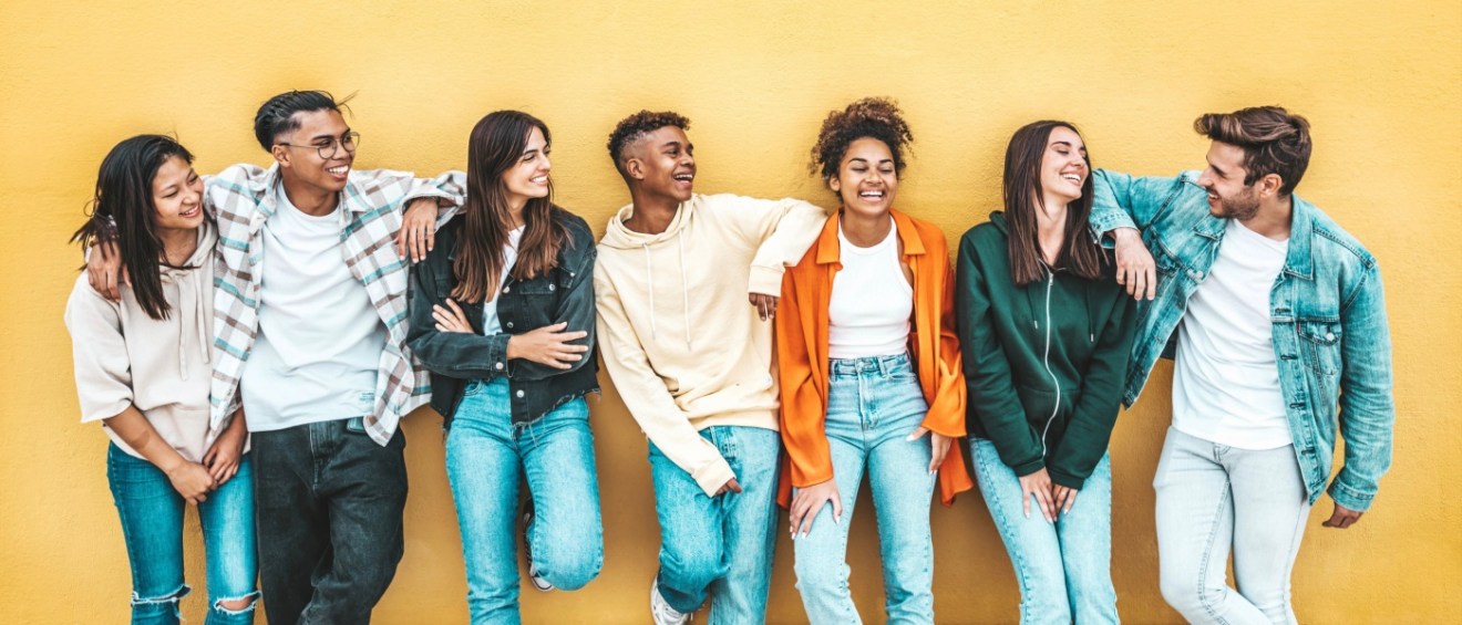 A diverse group of Gen Z friends leaning against a yellow wall, laughing and enjoying each other's company