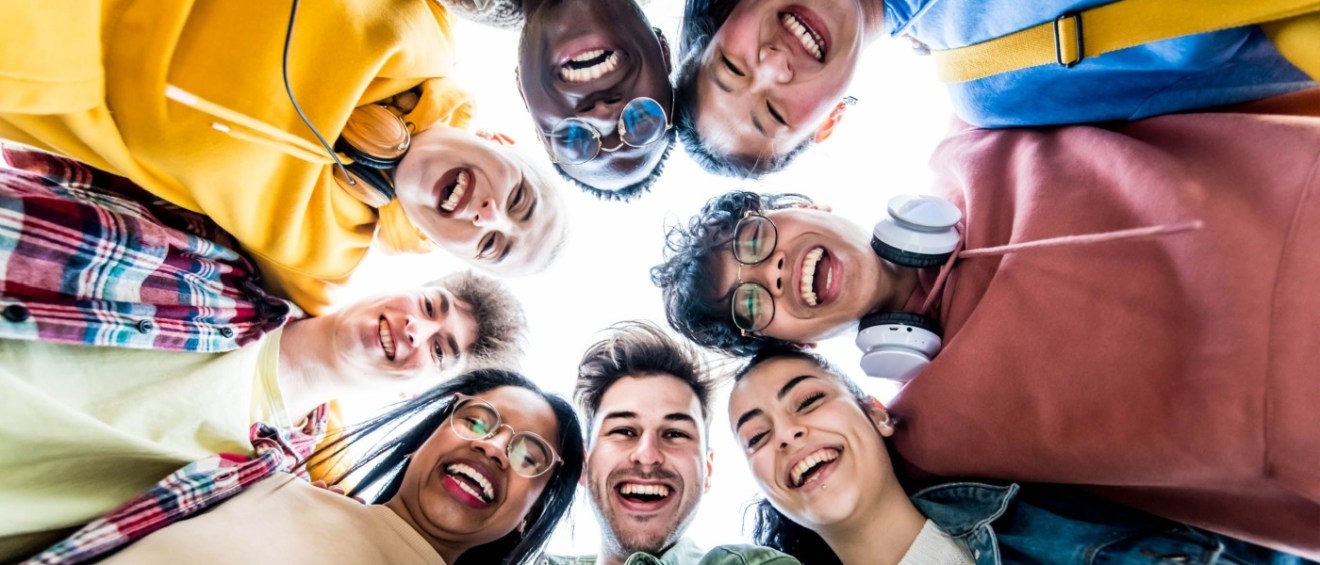Multiracial group of young people standing in a circle and smiling at the camera.