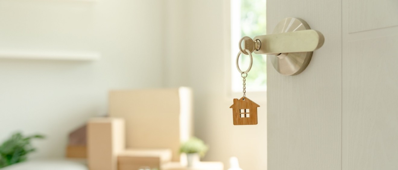 The door of a rental apartment that's move-in ready, with many boxes in the living room and a tiny house as a keychain.