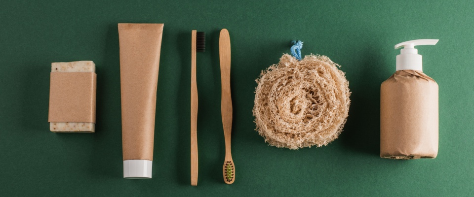 Handmade soap, toothpaste, bamboo toothbrushes, loofah sponge and shampoo on green background. Simple degradable package for eco-friendly bath products.