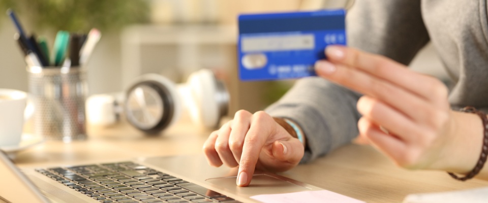 Close up of student girl hands paying rent online on her laptop with credit card sitting on a desk at home.