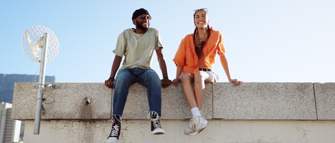 two gen z renters, a young man and young woman are sitting on a wall, smiling