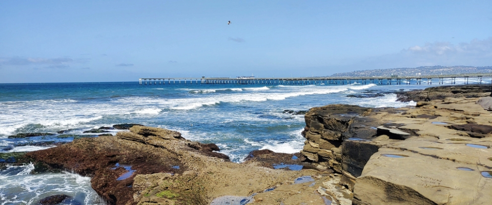 View of Ocean Beach in San Diego featuring rocky shoreline, ocean waves, and the Ocean Beach Pier, showcasing one of the city's top beaches for locals and renters.
