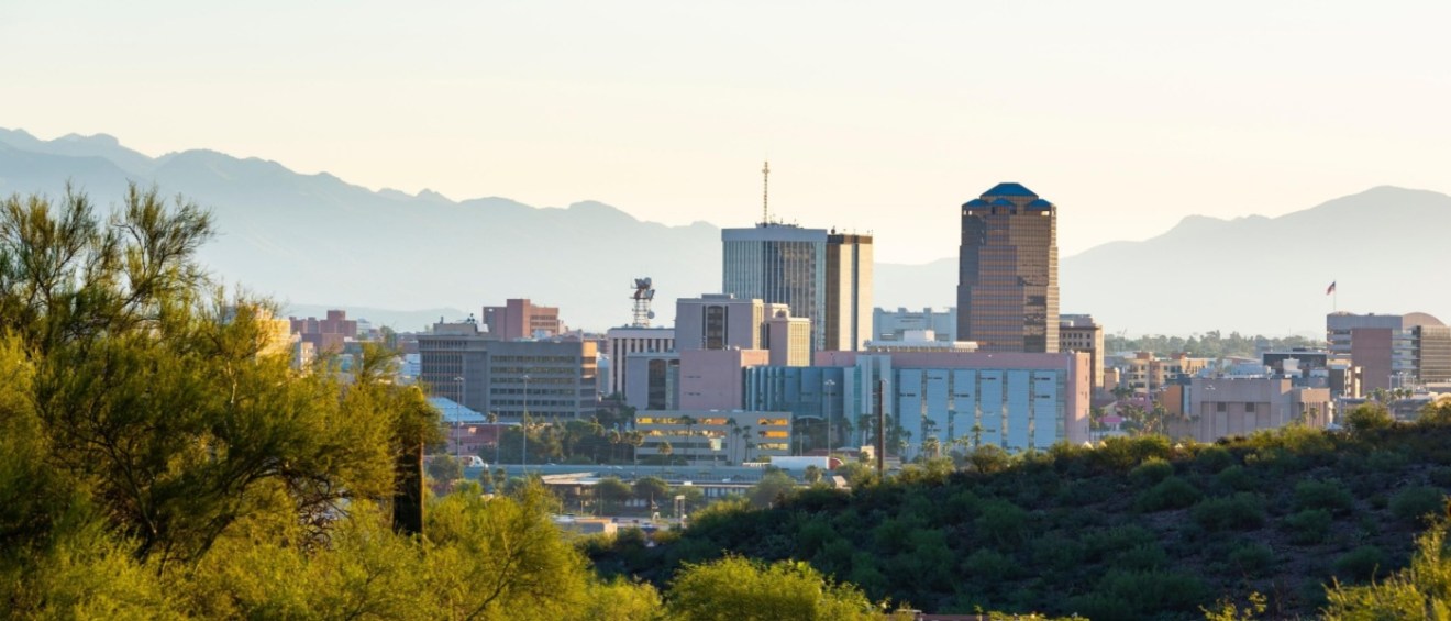 Skyline of Tucson, Arizona, with modern buildings set against a backdrop of mountains and desert vegetation in the foreground.