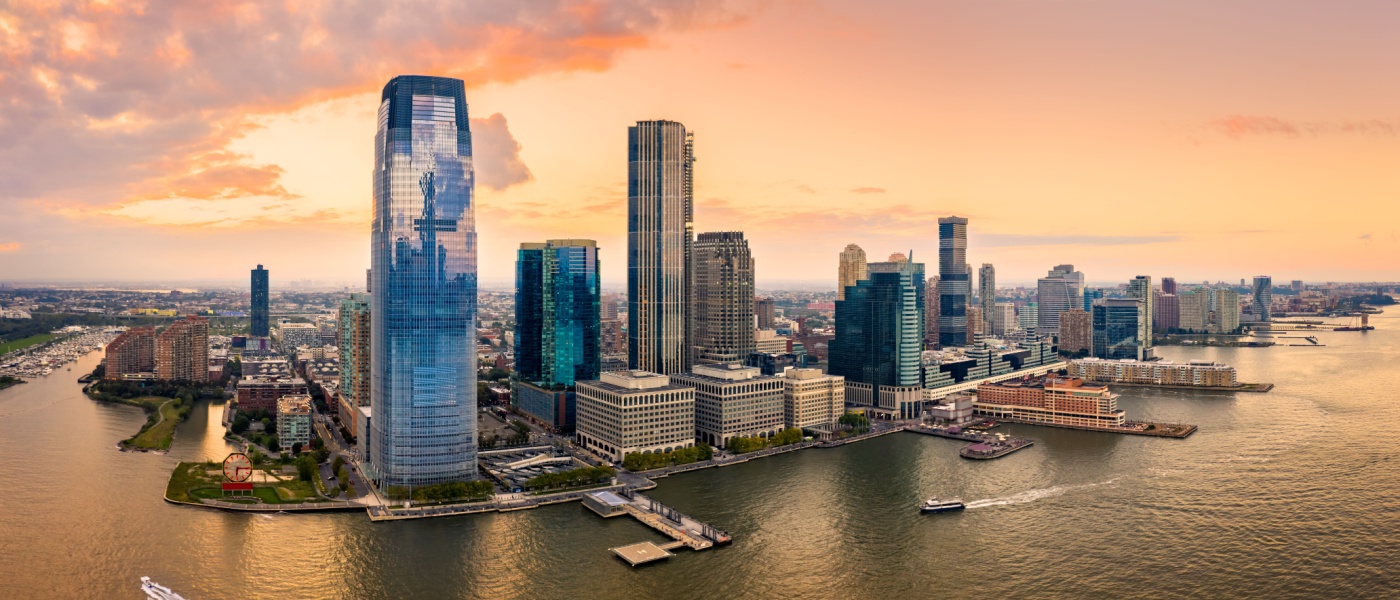 A stunning panoramic view of the Jersey City, NJ skyline at sunset, showcasing its towering skyscrapers and waterfront.