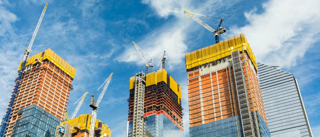Construction cranes tower over several high-rise buildings under development against a blue sky, showcasing the progress of a major apartment complex.