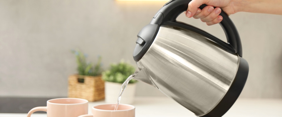 Woman pouring hot water from electric kettle into cup in kitchen.