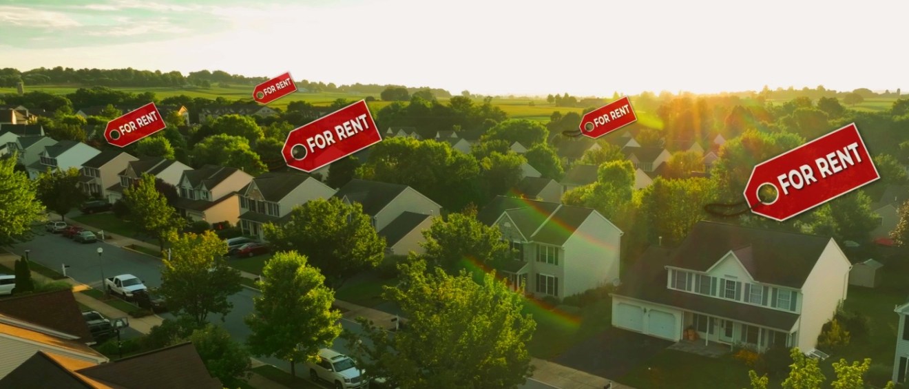 An aerial view of a suburban neighborhood with multiple houses, each displaying a prominent "For Rent" sign, representing a build-to-rent community with single-family homes available for rent.