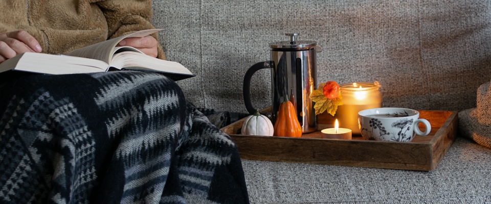 Picture of a woman spending a cozy autumn evening at home with comfortable sofa, warm plaid, aromatic tea, candles and interesting book.