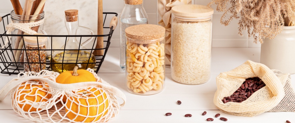 Assortment of grains, cereals and pasta in glass jars and kitchen utensils on wooden table.