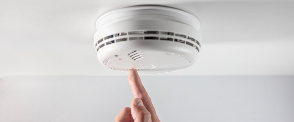 Man pushing the button on a home smoke and fire alarm detector. 