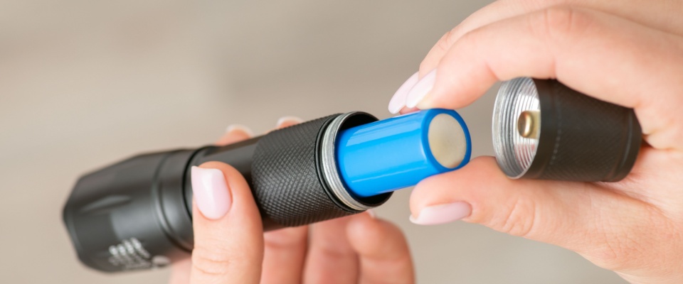 Flashlight with 18650 battery in female hands, close up. Small portable pocket device for lighting darkness at night.