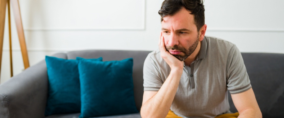 Man feeling lonely and upset while thinking about his problems sitting on the sofa at home.