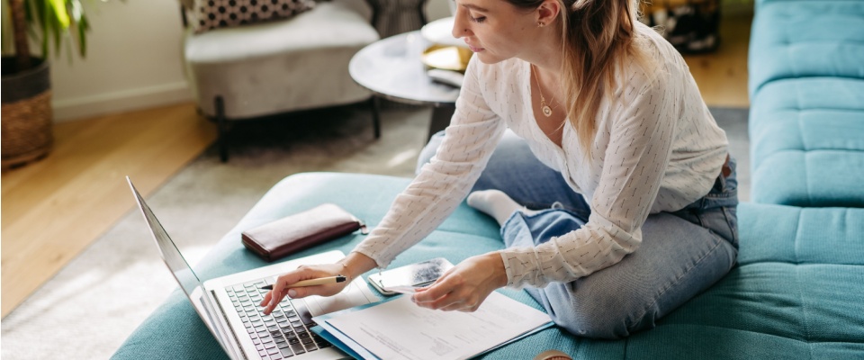 Woman paying bills online, sitting in living room, working on notebook.