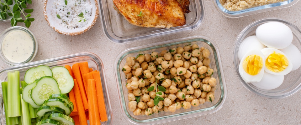 Glass containers with quinoa, chickpeas, eggs, and fresh vegetables ready for meal prepping.