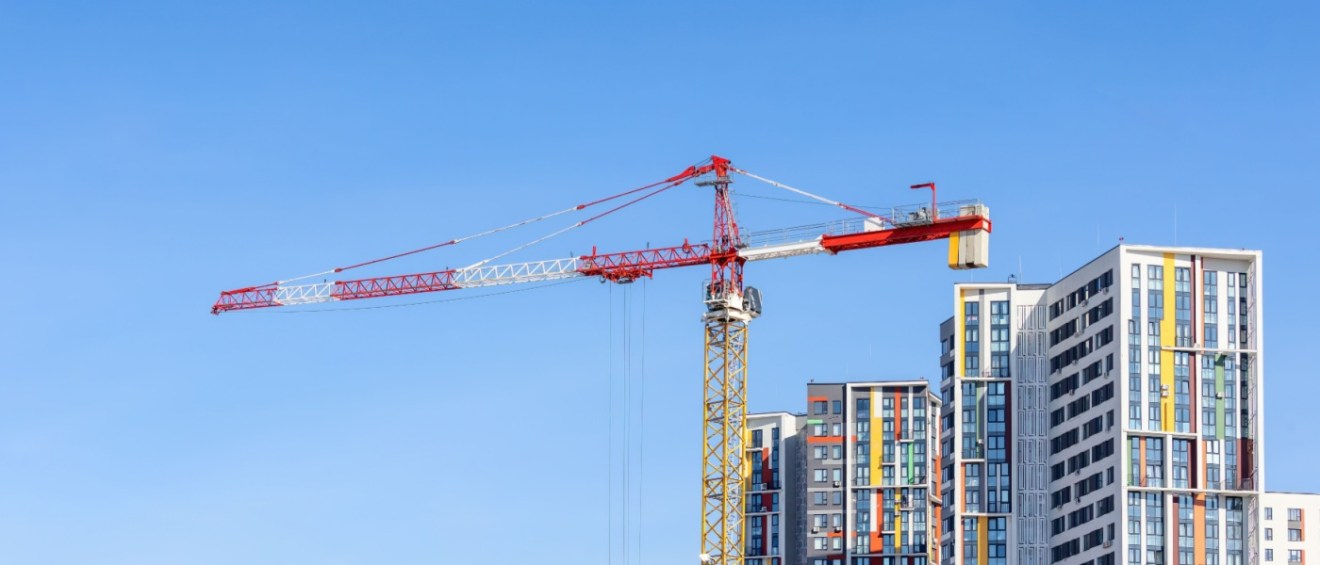 A construction crane working on a colorful, new apartment building under a clear blue sky.