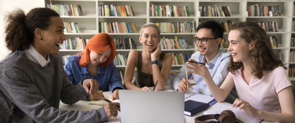 Diverse group of cheerful classmates brainstorming on common studying project in campus library.