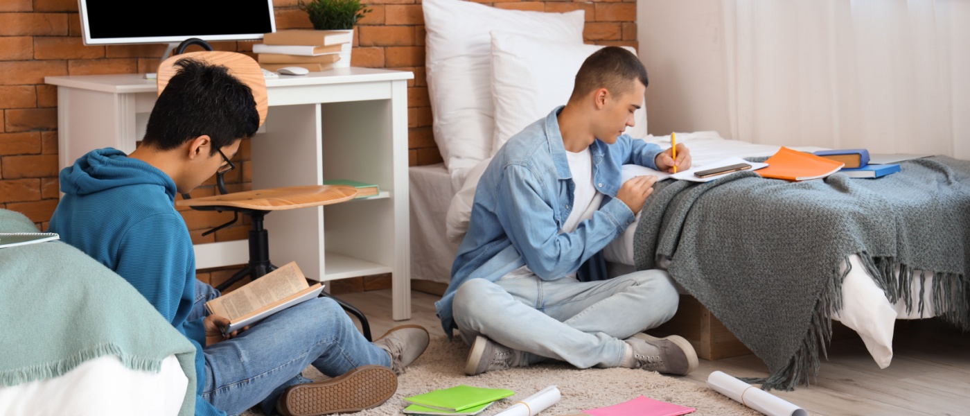 Two students studying on the floor in a cozy dorm room.