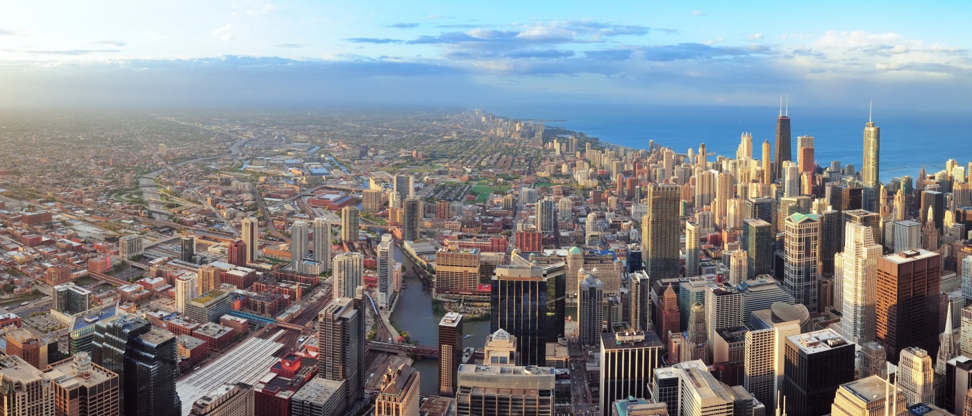 An aerial panorama captures the sprawling urban and suburban landscape of Chicago one of the hottest rental markets in the U.S. at the start of 2025 - showcasing its dense cluster of skyscrapers, including the iconic Willis Tower, transitioning into less concentrated development before meeting the vast expanse of Lake Michigan under a partially clouded sky.