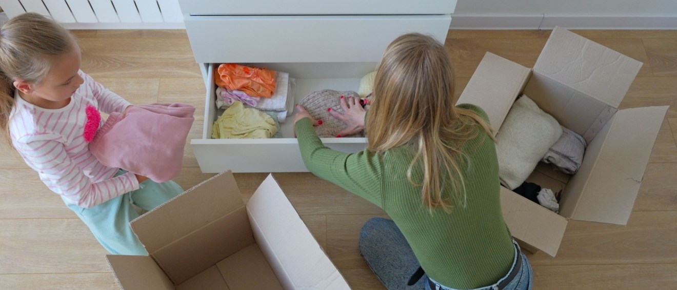 Little girl with mother taking out clothes from drawer in bedroom.