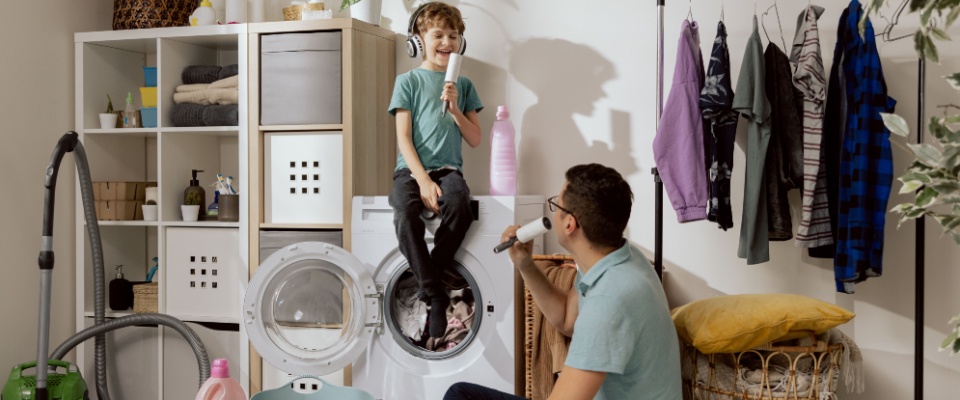 Father and son do household chores together, putting in laundry. 