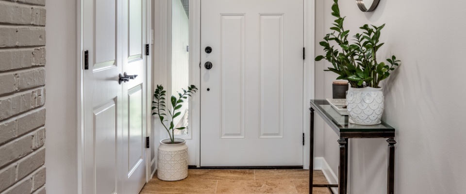 A cozy entryway with brown and brick walls, hardwood flooring, decorations, and a white front door with windows.