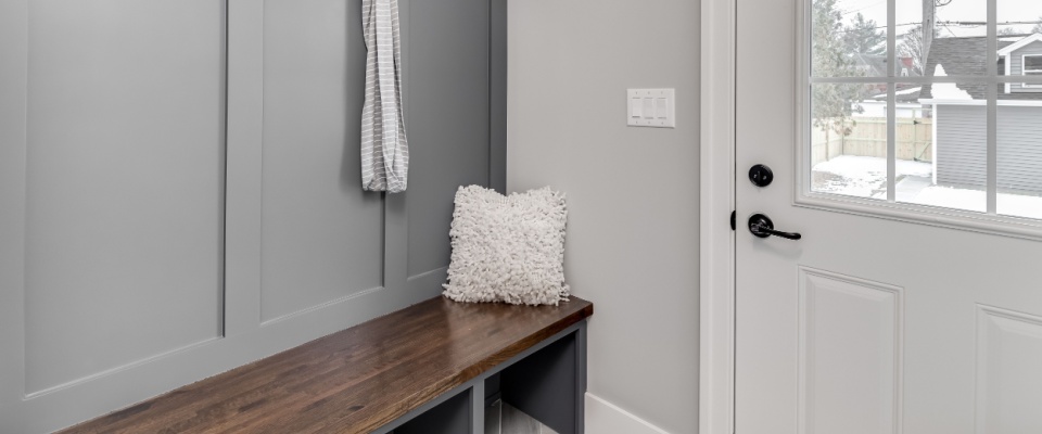 A staged detail shot of a gray mudroom entryway with bench seating, coat hooks, and storage above.