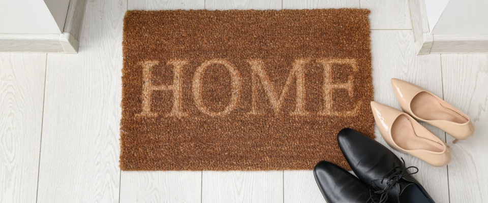 Door mat and shoes near doorway on white floor in hallway.