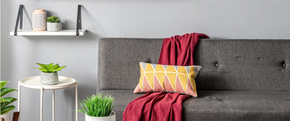 Modern living room interior with a grey armless sofa, a white round coffee table with wooden legs, and white floating shelves displaying decorative potted plants.