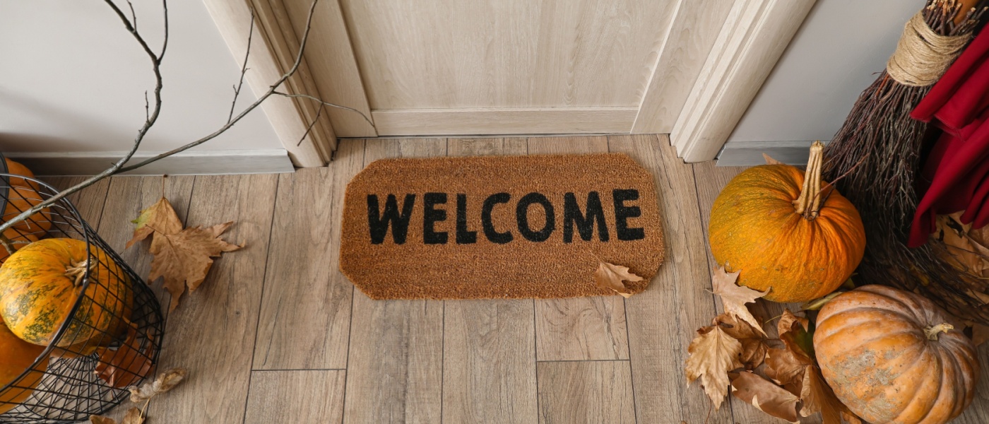 Door mat with Halloween pumpkins and fallen leaves in hall.
