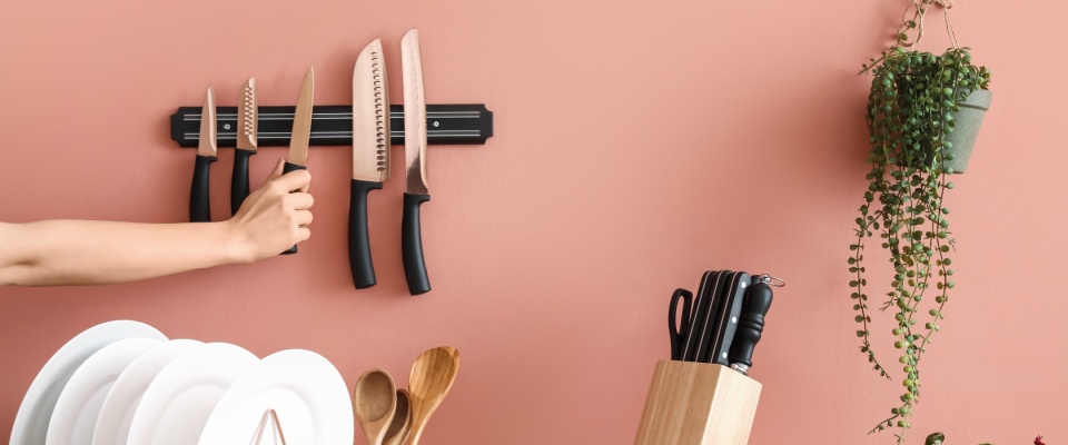 A woman in the kitchen surrounded by vegetables, with knives neatly organized on magnetic strips mounted on the wall.