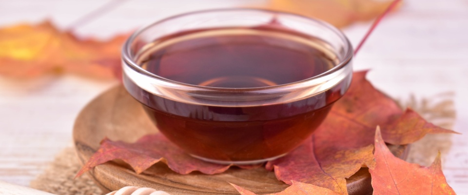 Close-up of maple syrup in a bowl, set against a backdrop of vibrant maple leaves.