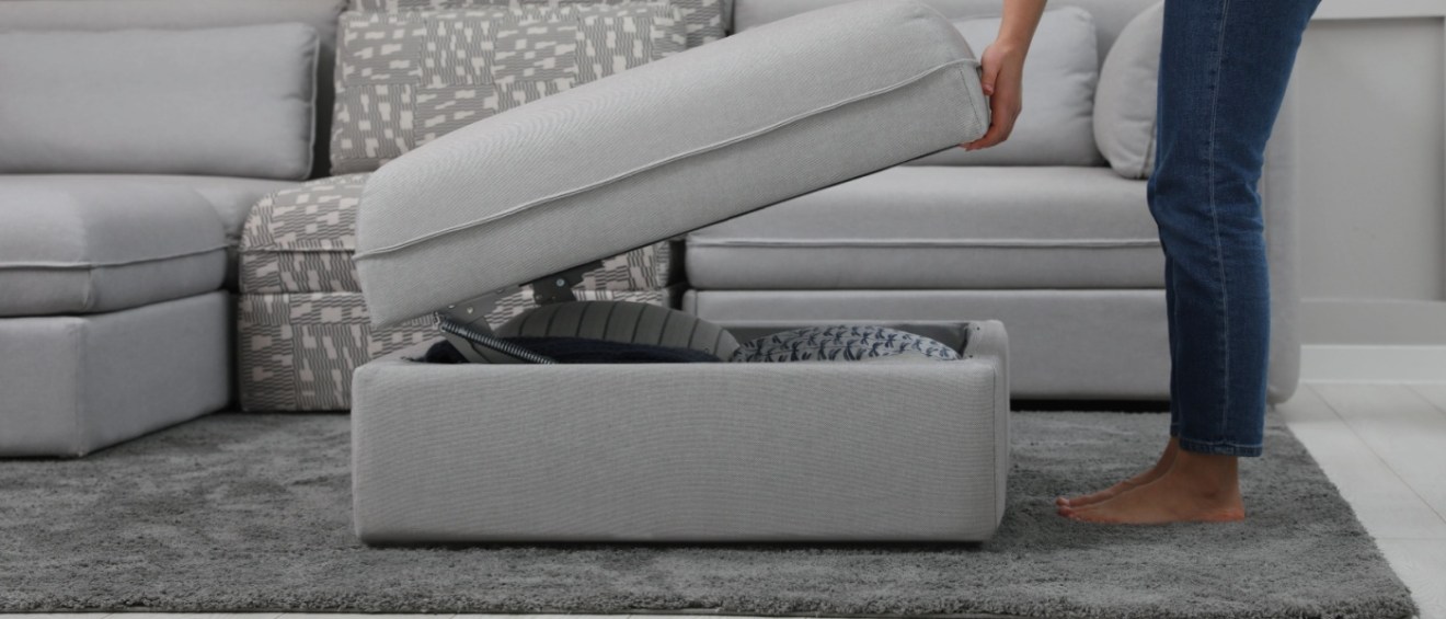 Close-up of a woman opening the storage compartment of a modular sofa in a living room, revealing a practical hidden space