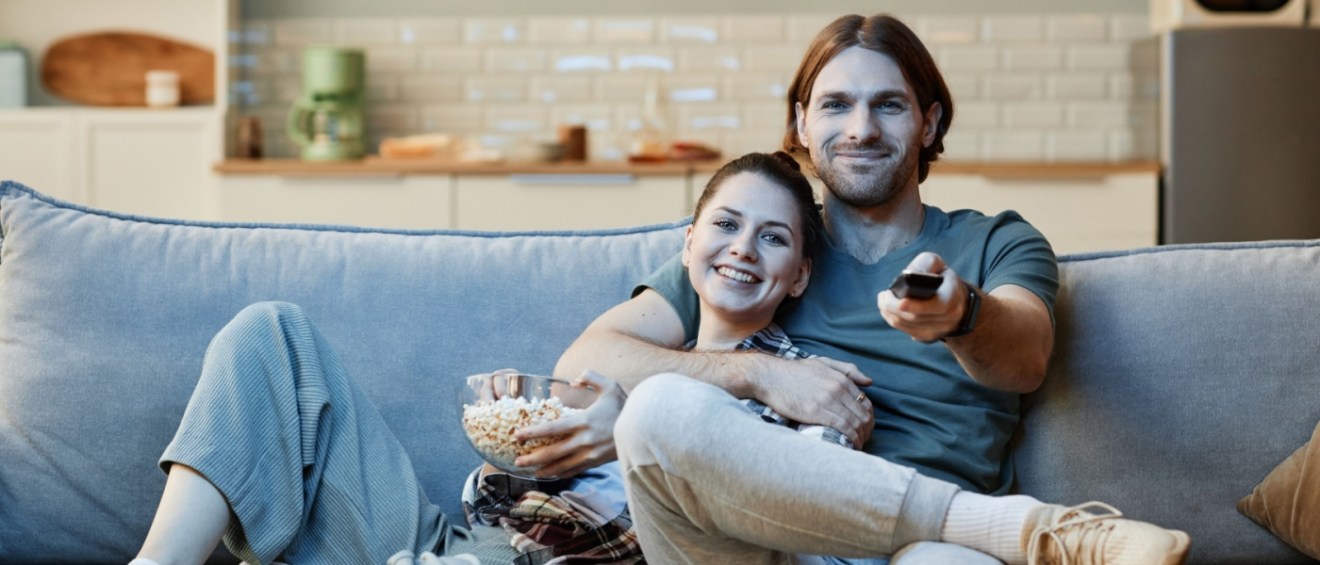 A couple of renters relaxing on the couch, watching blockbuster movies, with a bowl of popcorn and a remote in hand.