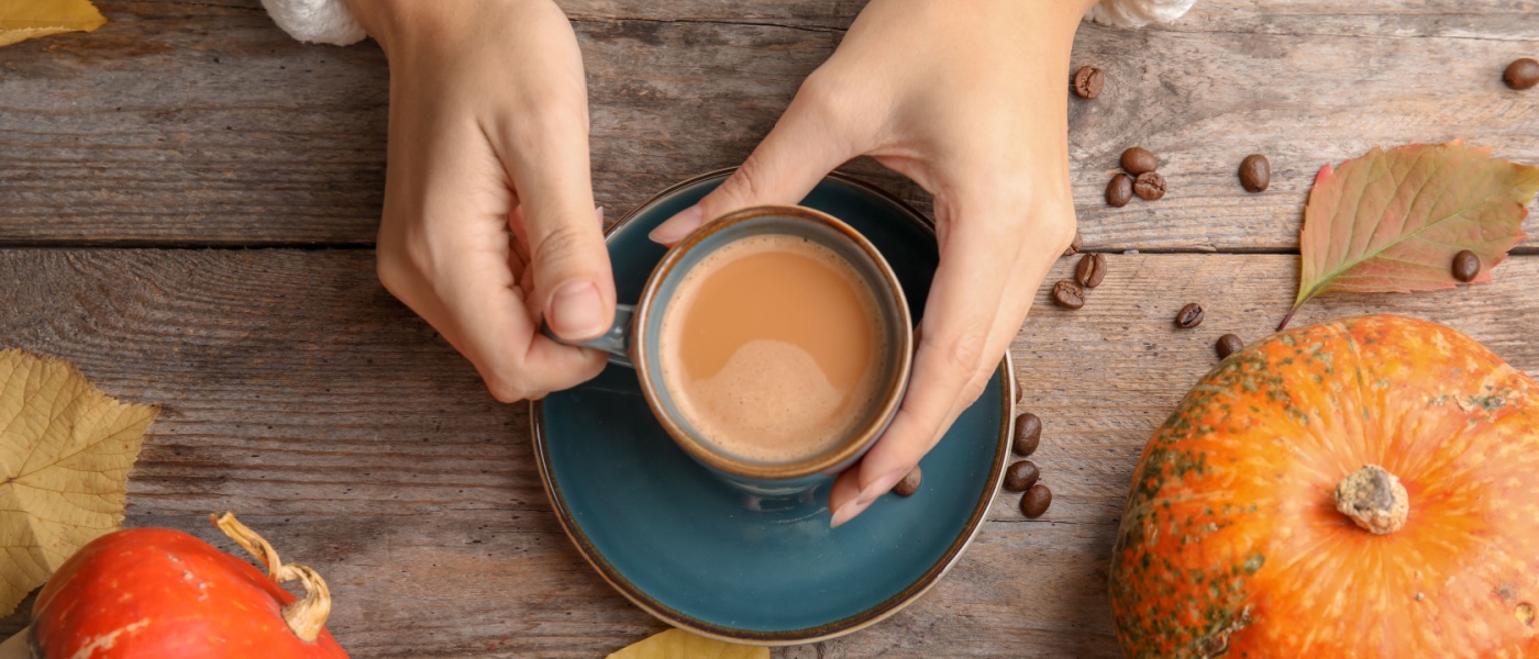 Woman holding cup of tasty pumpkin spice latte on a wooden table.